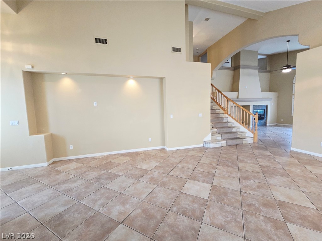 1265 Moon Vision Street Henderson, NV 89052 - Photo 9 of 35 Unfurnished living room featuring a glass covered fireplace, light tile patterned floors, a ceiling fan, and arched walkways
