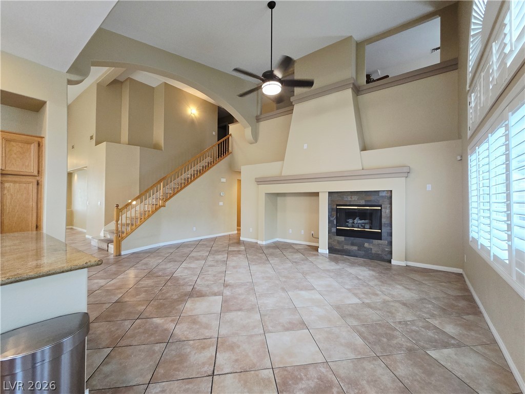 1265 Moon Vision Street Henderson, NV 89052 - Photo 10 of 35 Unfurnished living room featuring a ceiling fan, a high ceiling, a fireplace, and light tile patterned flooring