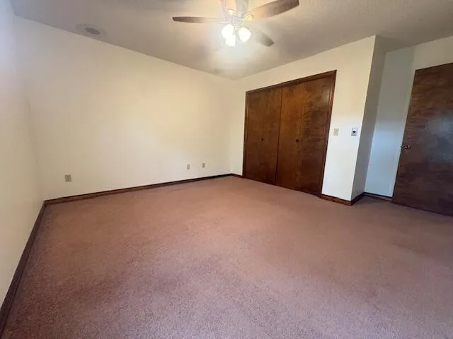 an empty room with a ceiling fan and closet area