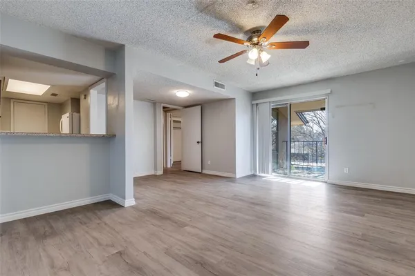 a view of an empty room with wooden floor and a ceiling fan