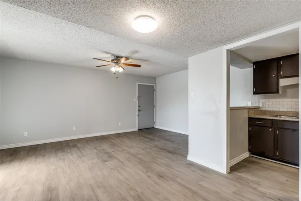 a view of an empty room and kitchen with wooden floor