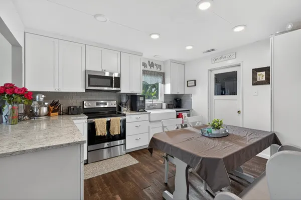 a kitchen with stainless steel appliances granite countertop a stove top oven a sink dishwasher a dining table and chairs with wooden floor