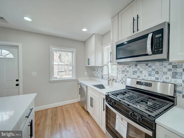 a kitchen with white cabinets a sink a stove a refrigerator and a stove with wooden floor