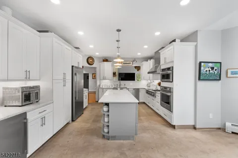 a large white kitchen with stainless steel appliances kitchen island a stove a refrigerator a oven and a cabinets