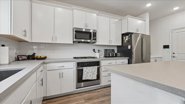 a kitchen with stainless steel appliances granite countertop white cabinets a sink a stove a refrigerator and microwave with wooden floor