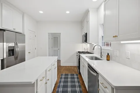 a kitchen with stainless steel appliances a stove a sink a refrigerator white cabinets and wooden floor