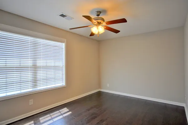 an empty room with wooden floor fan and windows
