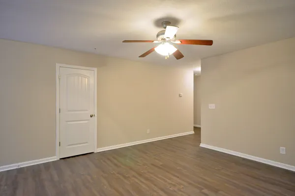 an empty room with wooden floor fan and windows