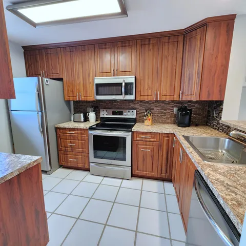 a kitchen with stainless steel appliances granite countertop a stove top oven a sink dishwasher and a refrigerator with wooden cabinets