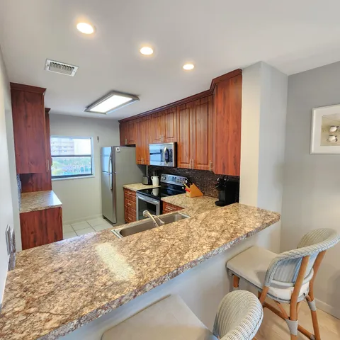 a kitchen with stainless steel appliances granite countertop wooden cabinets a stove top oven a granite counter tops and a view of living room