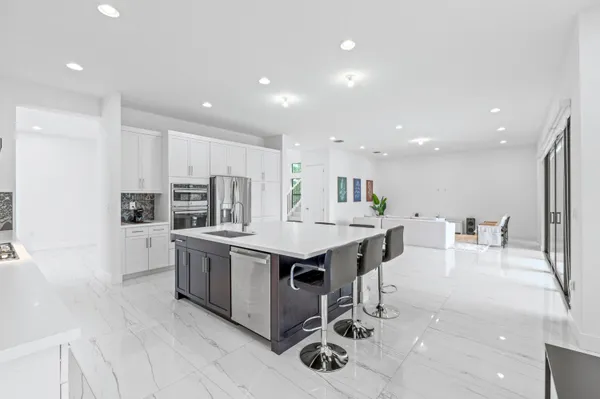 a large white kitchen with stainless steel appliances kitchen island granite countertop a refrigerator and cabinets