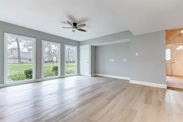 a view of an empty room with wooden floor and a ceiling fan