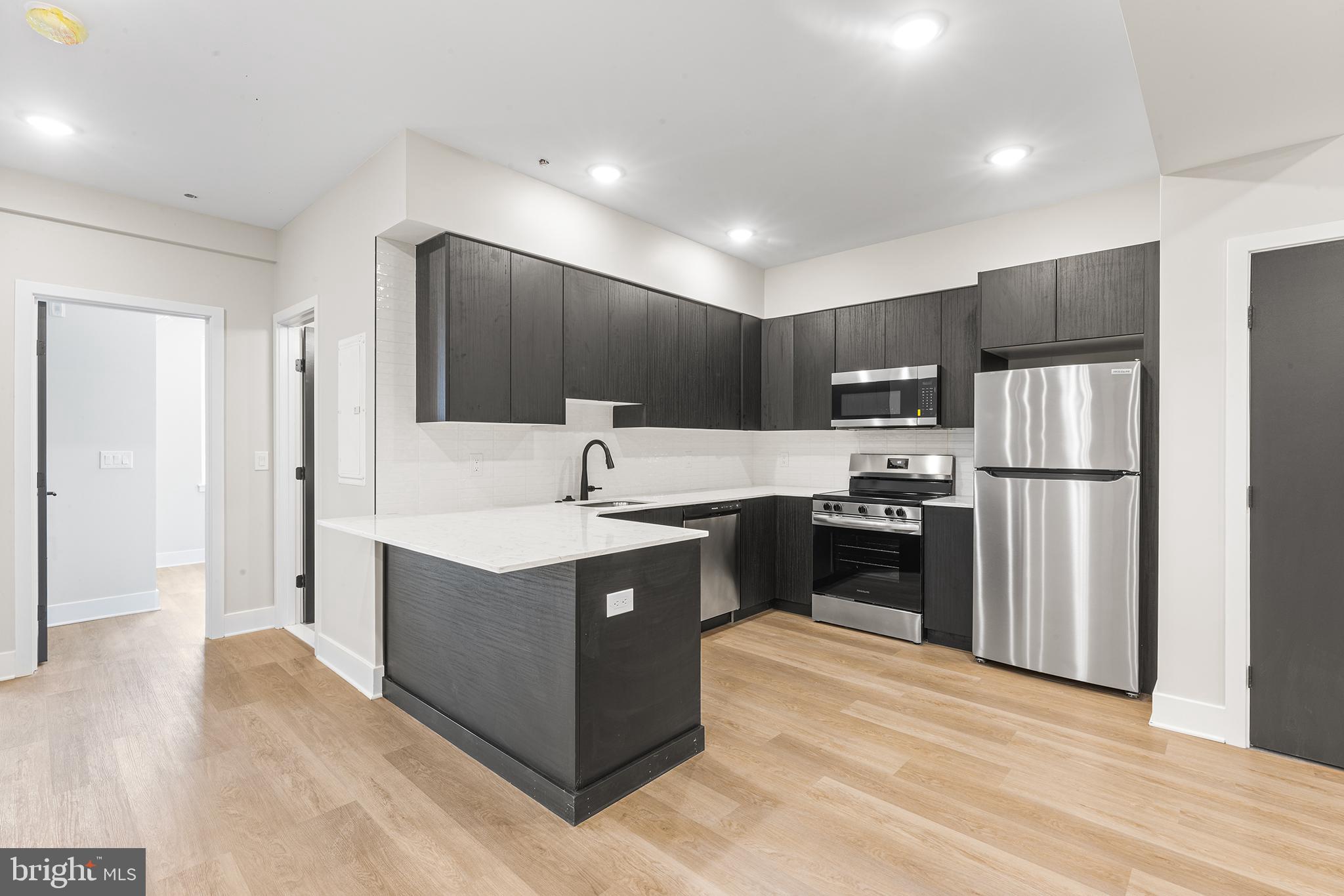 1903 Jackson Street, Unit 1 Philadelphia, PA 19145 - Photo 5 of 17 a kitchen with kitchen island a refrigerator stove a sink and dishwasher with wooden floor