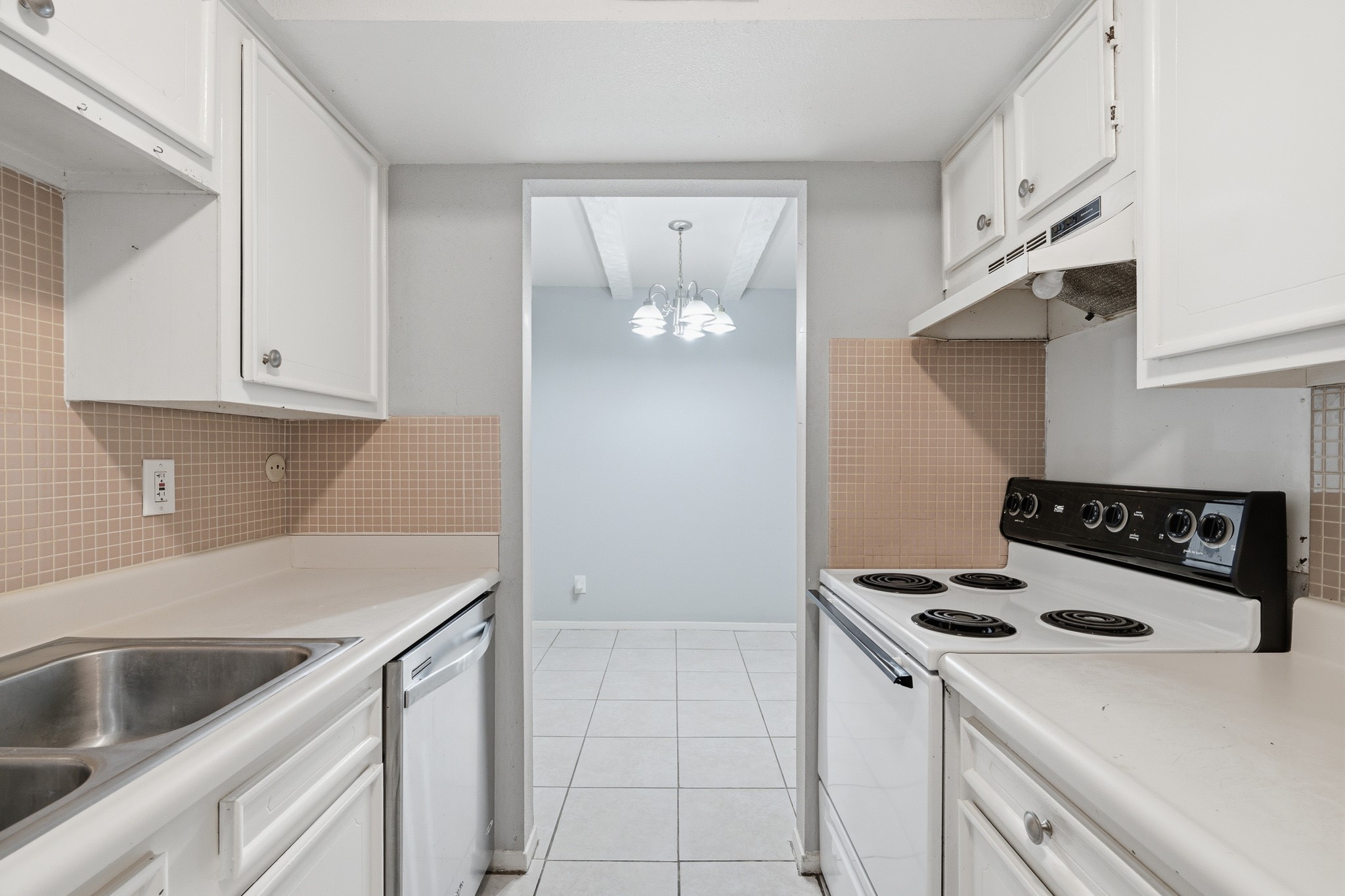 11550 Chimney Rock Road, Unit 133 Houston, TX 77035 - Photo 14 of 40 Charming galley kitchen with white cabinetry, tiled backsplash, and a cozy dining area view, featuring an electric stove and dishwasher for convenient meal preparation.