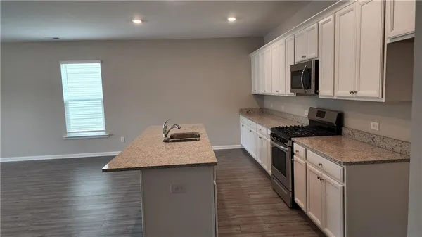 a kitchen with kitchen island granite countertop a sink a stove top oven a counter space and cabinets