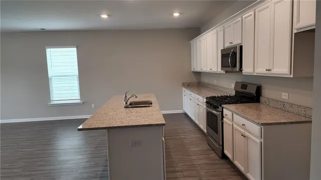 a kitchen with kitchen island granite countertop a sink a stove top oven a counter space and cabinets