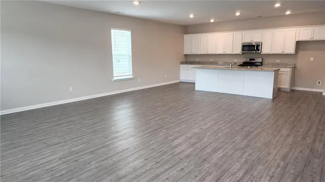 a kitchen with stainless steel appliances granite countertop a sink a microwave a refrigerator and white cabinets with wooden floor