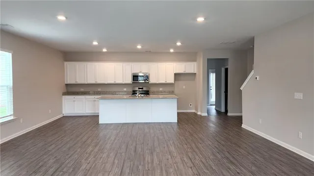 a view of kitchen with granite countertop refrigerator oven a sink dishwasher and white cabinets with wooden floor