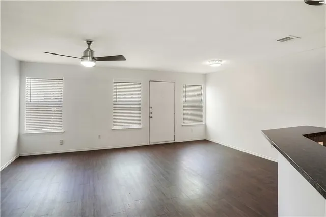 a view of an empty room with wooden floor and a ceiling fan