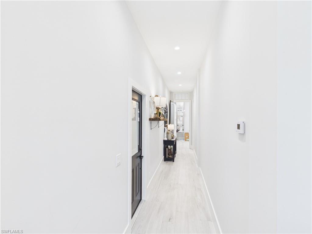 3650 Sunset Boulevard Naples, FL 34112 - Photo 16 of 26 Hallway featuring recessed lighting, light wood-finish flooring, white walls, and a black paneled door