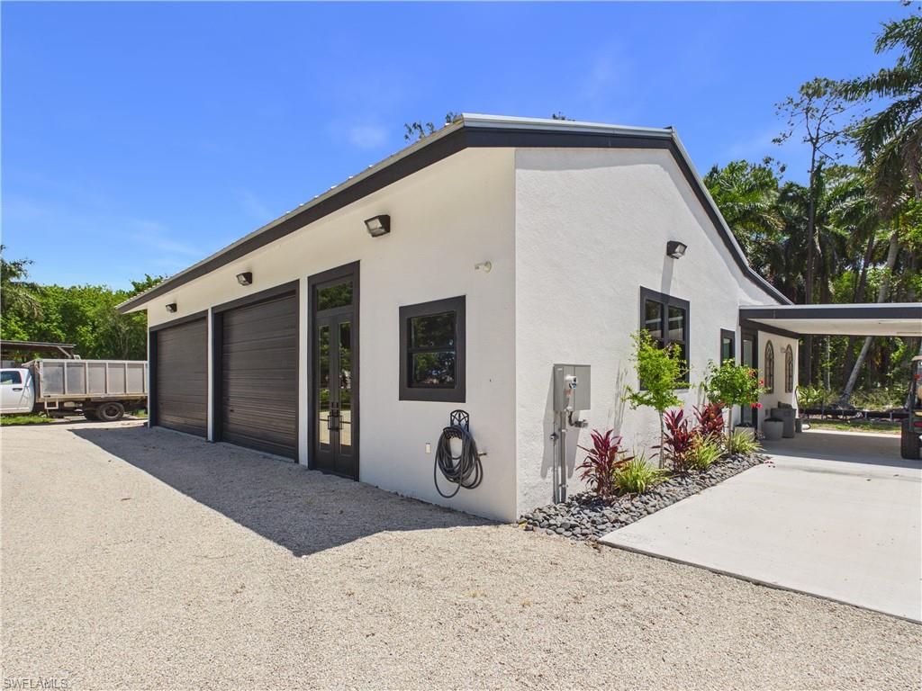 3650 Sunset Boulevard Naples, FL 34112 - Photo 2 of 26 Modern white stucco exterior with a multi-car garage featuring dark wood-look doors, a covered carport, and accent landscaping