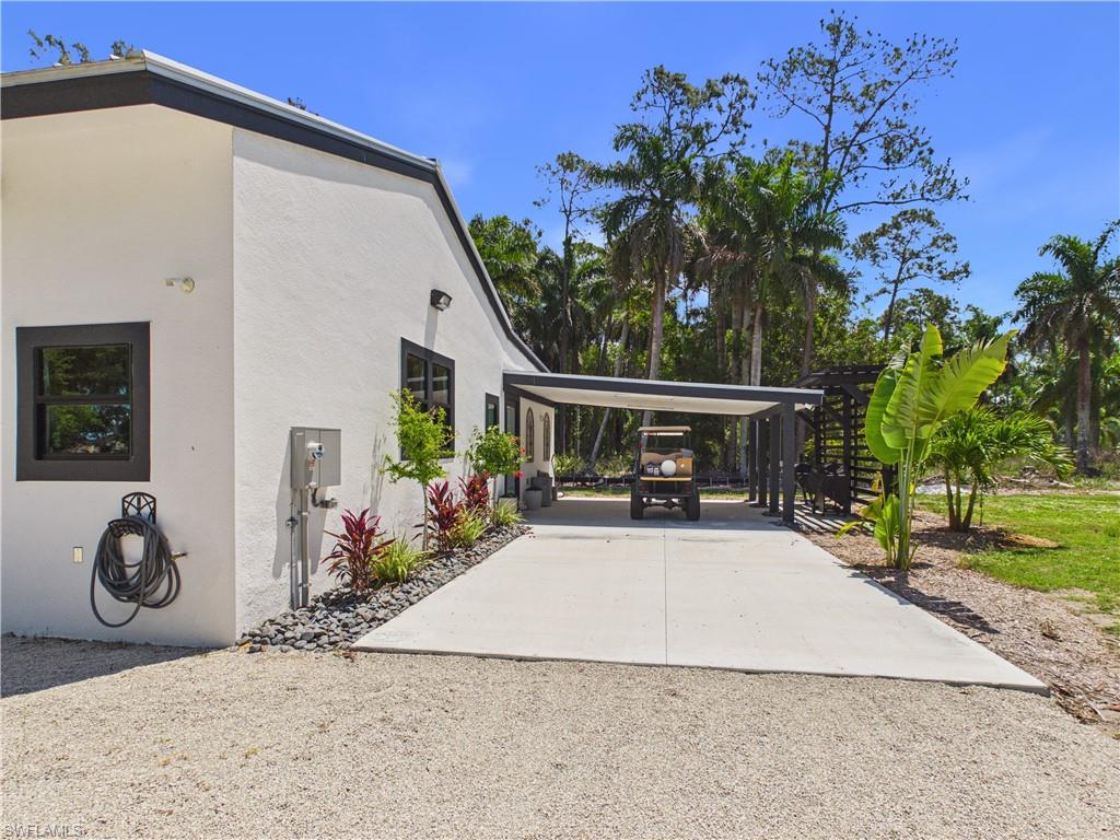 3650 Sunset Boulevard Naples, FL 34112 - Photo 26 of 26 White stucco exterior with black-framed windows, a covered carport, and a gravel driveway