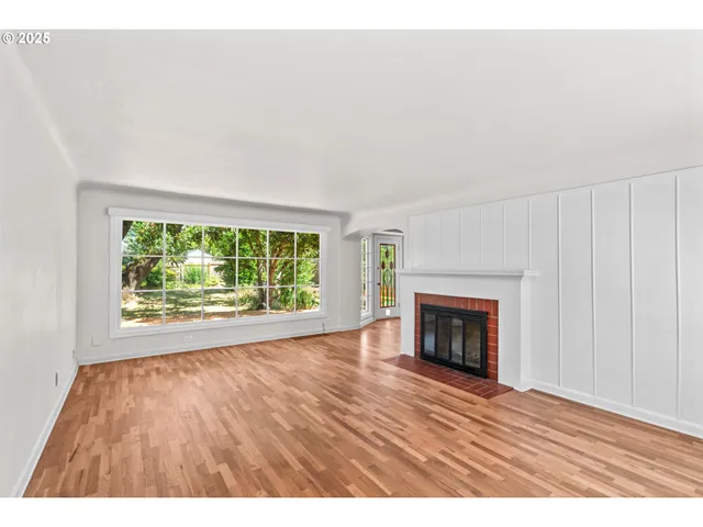 a view of an empty room with wooden floor fireplace and a window
