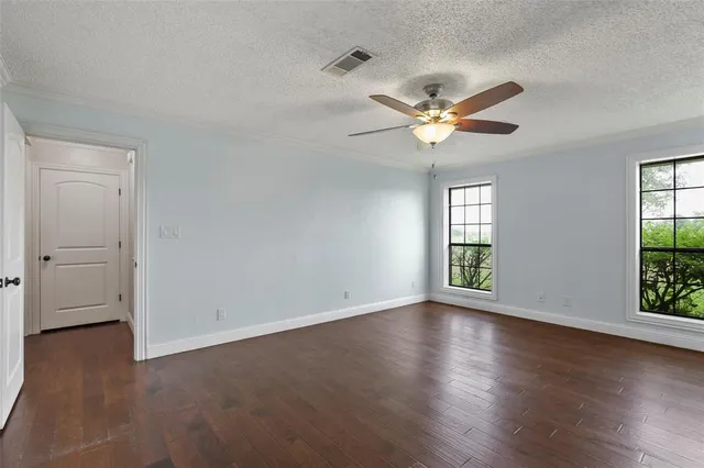 an empty room with wooden floor chandelier fan and windows