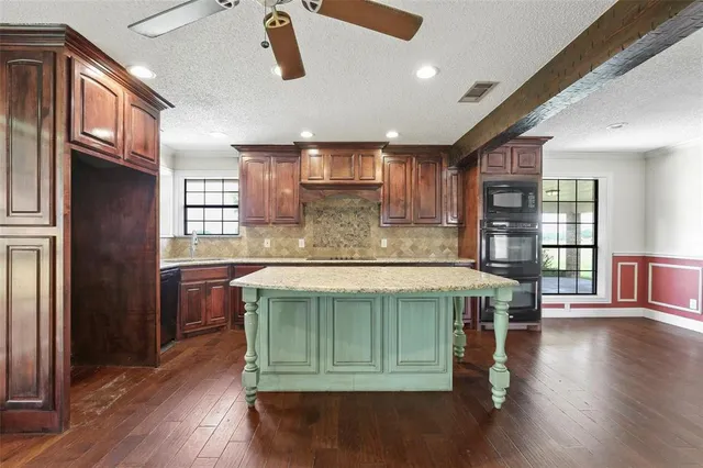 a kitchen with kitchen island granite countertop wooden floors and a view of living room