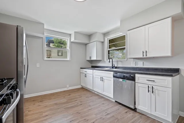 a kitchen with stainless steel appliances granite countertop a stove a sink and white cabinets with wooden floor