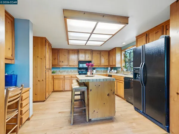 a kitchen with stainless steel appliances granite countertop a refrigerator a sink dishwasher a stove and a dining table with wooden cabinet