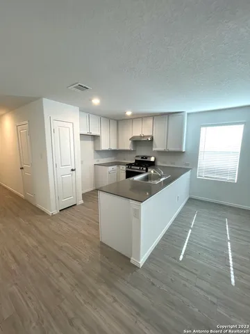 a kitchen with wooden floors white cabinets appliances and a window