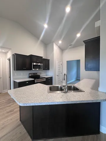 a kitchen with kitchen island granite countertop a sink and a stove top oven with wooden floor