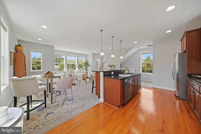 a kitchen with stainless steel appliances kitchen island granite countertop a refrigerator a stove a sink a dining table and chairs with wooden floor