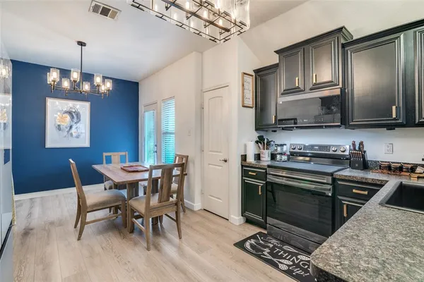 a kitchen with stainless steel appliances granite countertop a stove a refrigerator a sink a dining table and chairs with wooden floor