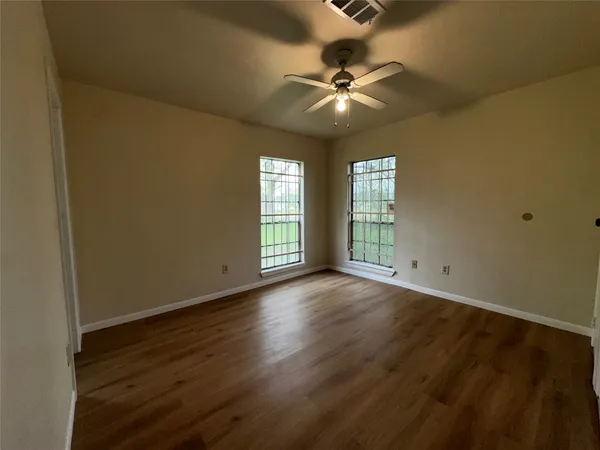 an empty room with wooden floor fan and windows