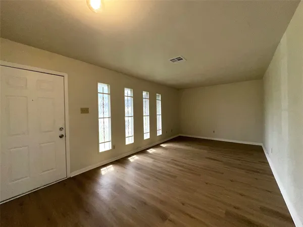 a view of an empty room with wooden floor and a window