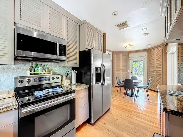a kitchen with stainless steel appliances kitchen island granite countertop a refrigerator a stove top oven and a dining table with wooden floor