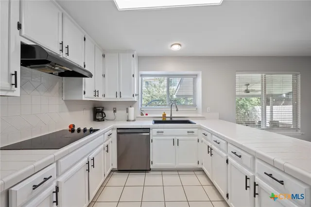 a kitchen with white cabinets appliances a sink and a window