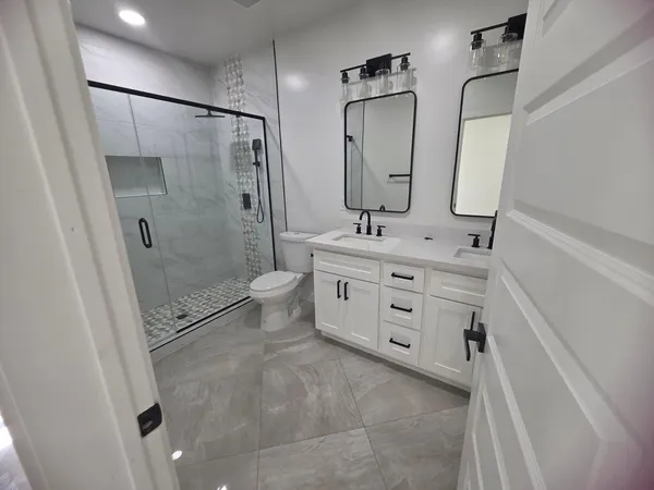 a bathroom with a double vanity sink toilet mirror and shower