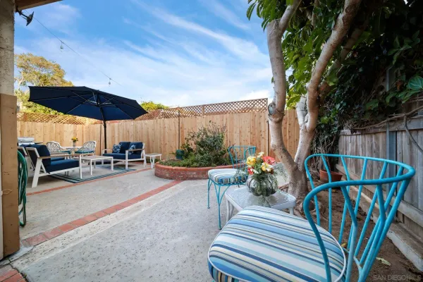 a view of a patio with couches table and chairs under an umbrella with a small yard
