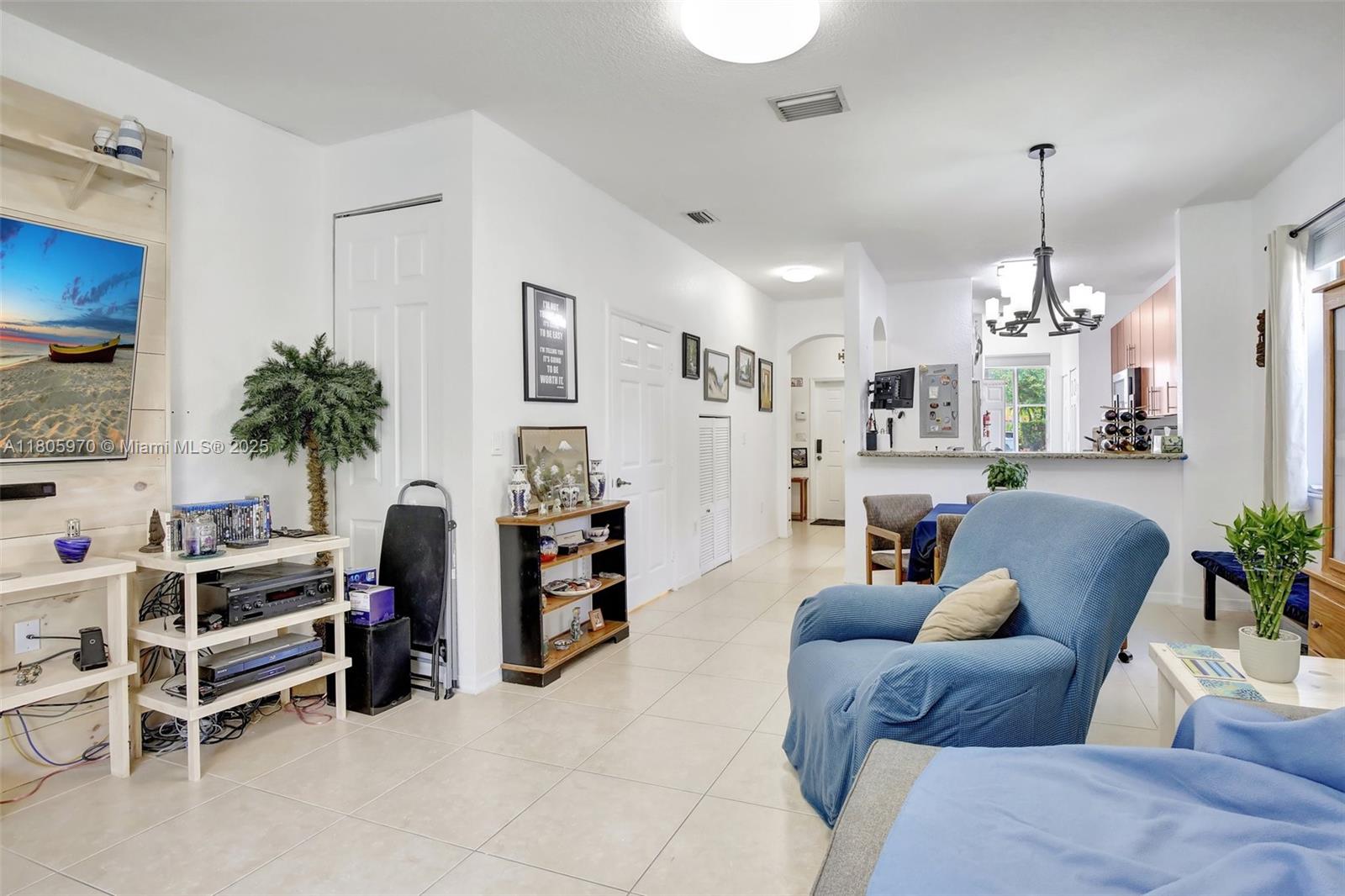 8999 Southwest 18th Street, Unit 1401 Miramar, FL 33025 - Photo 34 of 51 a living room with furniture a chandelier and a flat screen tv