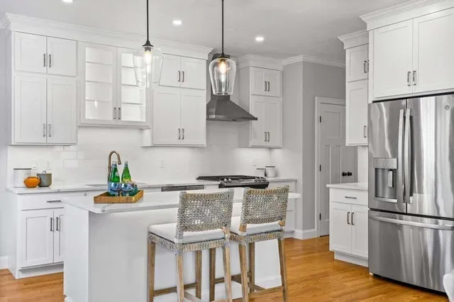 a kitchen with stainless steel appliances granite countertop a refrigerator a stove a sink and white cabinets with wooden floor