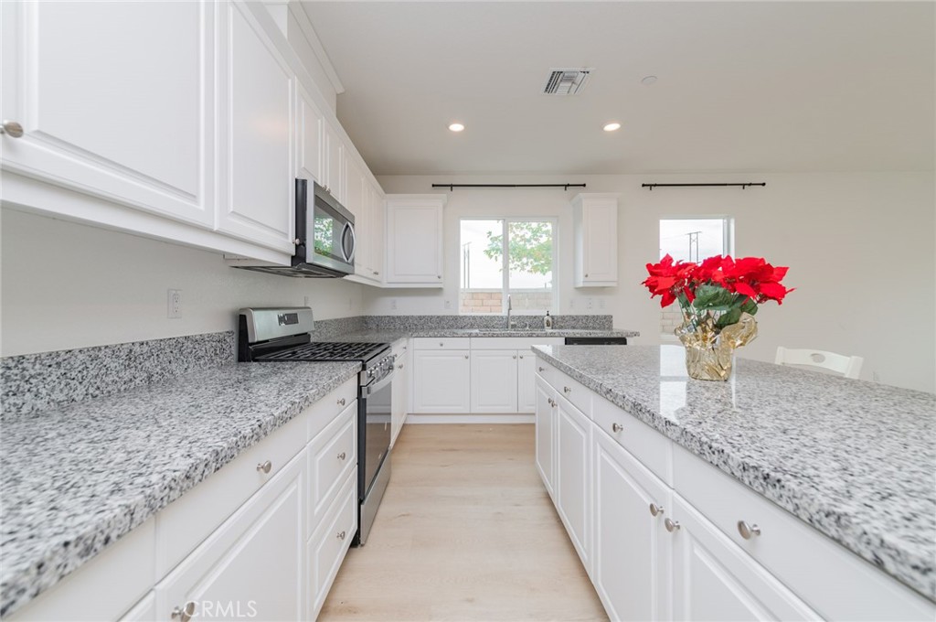 7309 Grazing Lane Riverside, CA 92507 - Photo 27 of 43 a large kitchen with granite countertop a sink flowers oven and white cabinets