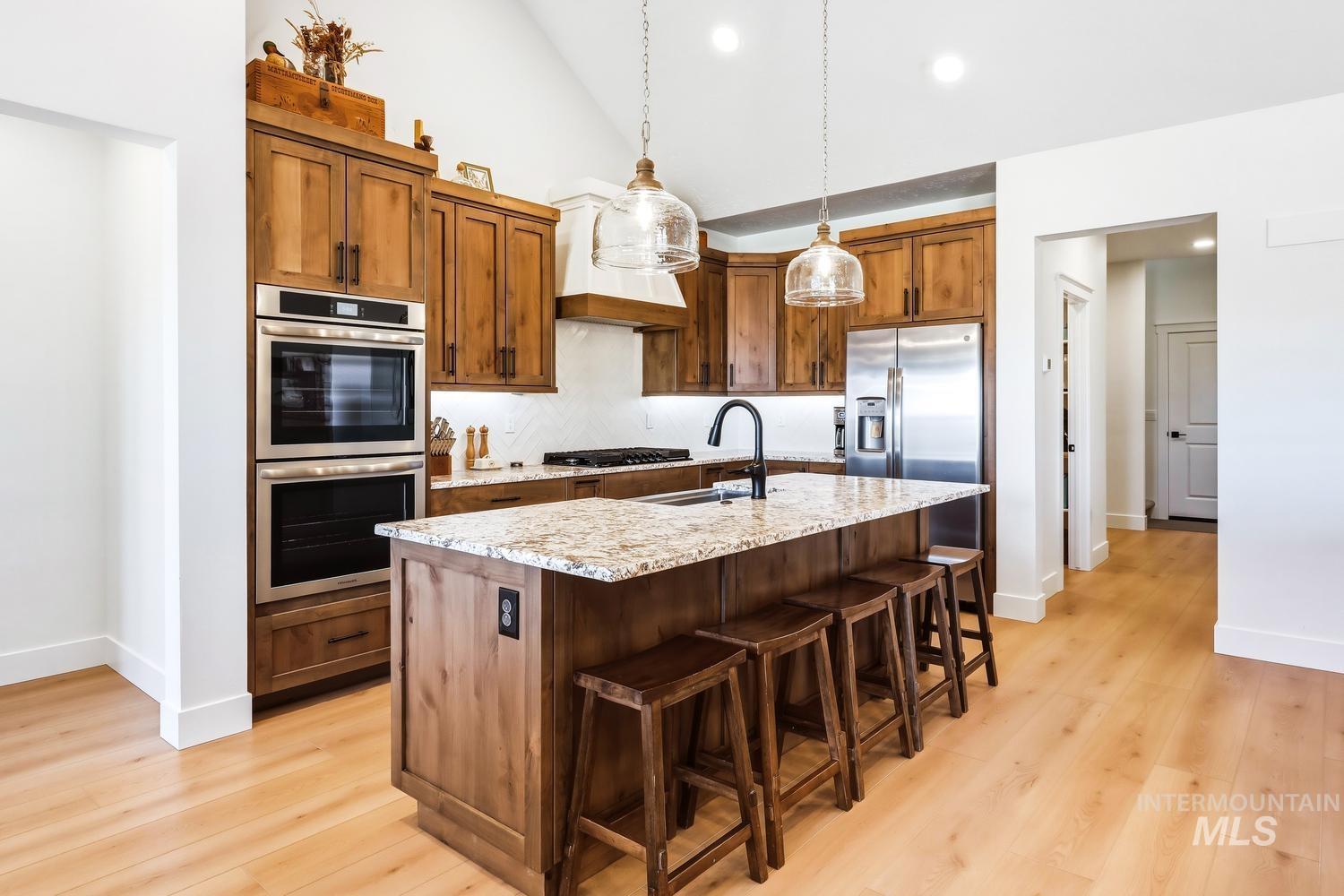 18658 Tranquil Place Caldwell, ID 83607 - Photo 11 of 44 Kitchen featuring wood cabinetry, light wood-finish flooring, a large island with a stone countertop, stainless steel appliances, and pendant lighting