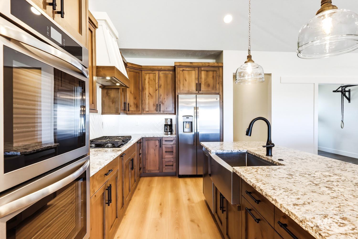 18658 Tranquil Place Caldwell, ID 83607 - Photo 13 of 44 Gourmet kitchen featuring a stainless steel double oven, gas cooktop, farmhouse sink, wood-finish cabinetry, and light-toned countertops