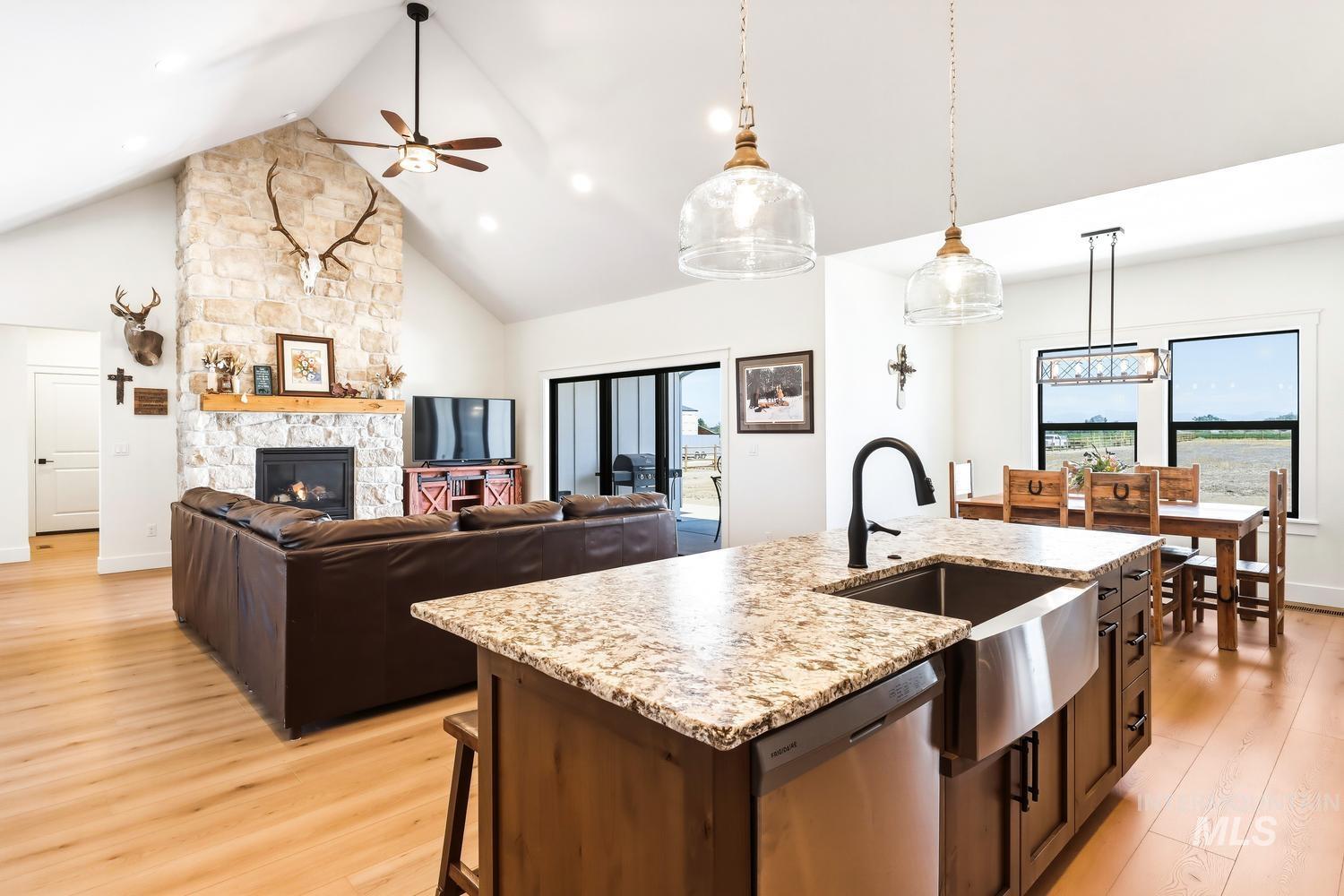 18658 Tranquil Place Caldwell, ID 83607 - Photo 14 of 44 Open-concept living space featuring vaulted ceilings, a stone-clad fireplace with a wood mantle, wood-finish flooring, and a kitchen island with granite countertops and a farmhouse sink