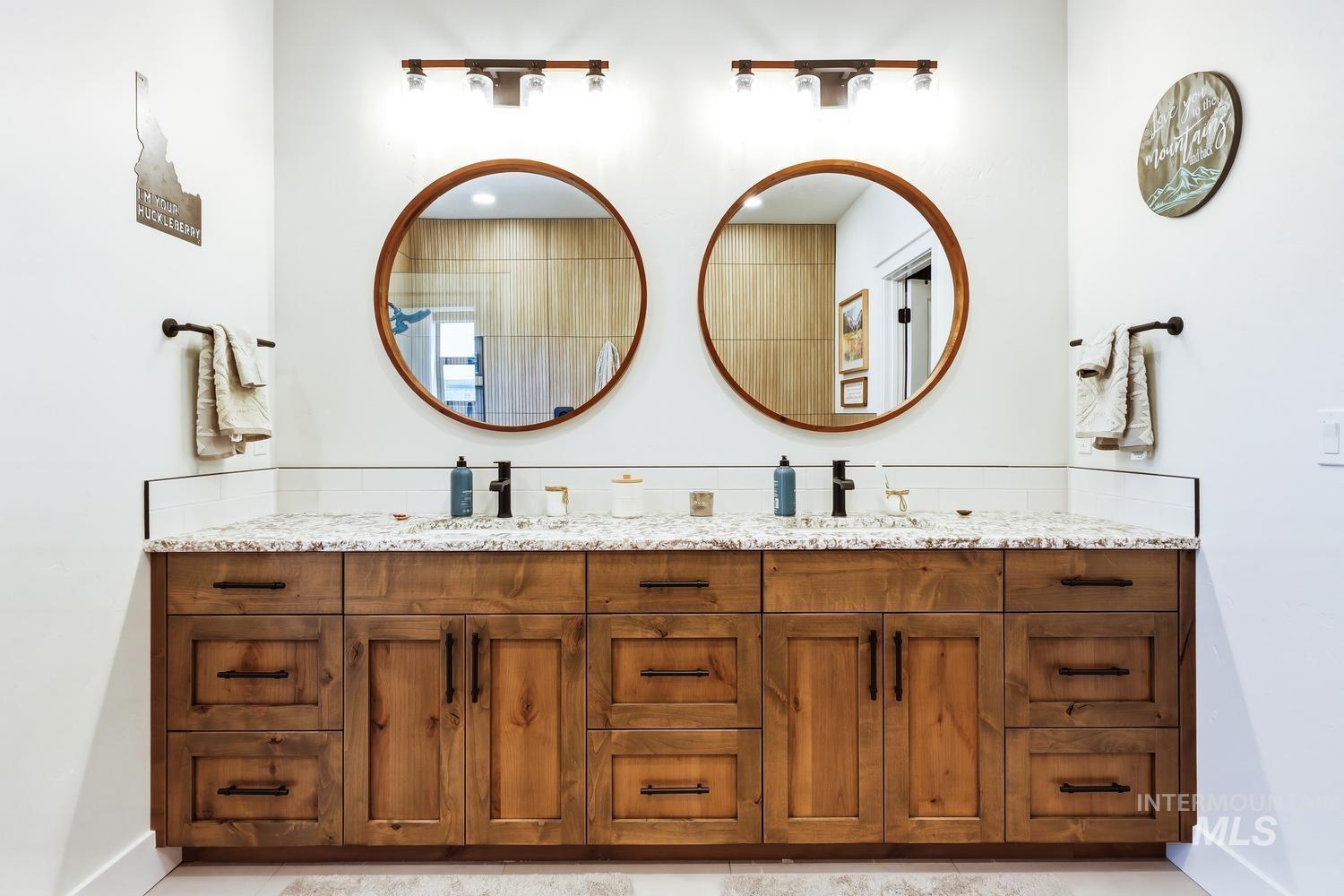 18658 Tranquil Place Caldwell, ID 83607 - Photo 24 of 44 Dual wood-finish vanity with granite-style countertop, two round framed mirrors, matte black fixtures, and integrated lighting