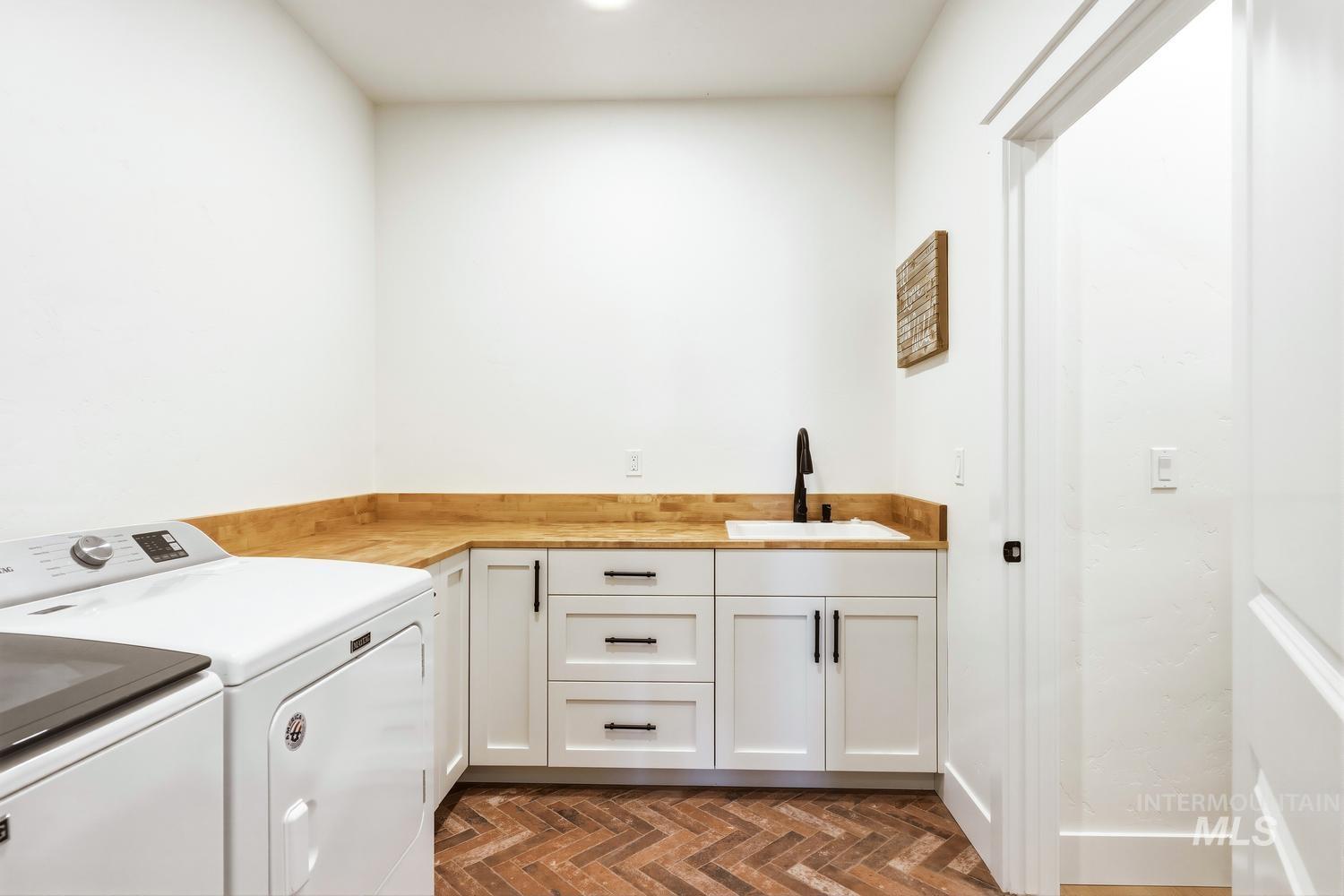 18658 Tranquil Place Caldwell, ID 83607 - Photo 39 of 44 Laundry room featuring white cabinetry, wood-finish countertops, a utility sink with a matte black faucet, and herringbone-patterned brick flooring