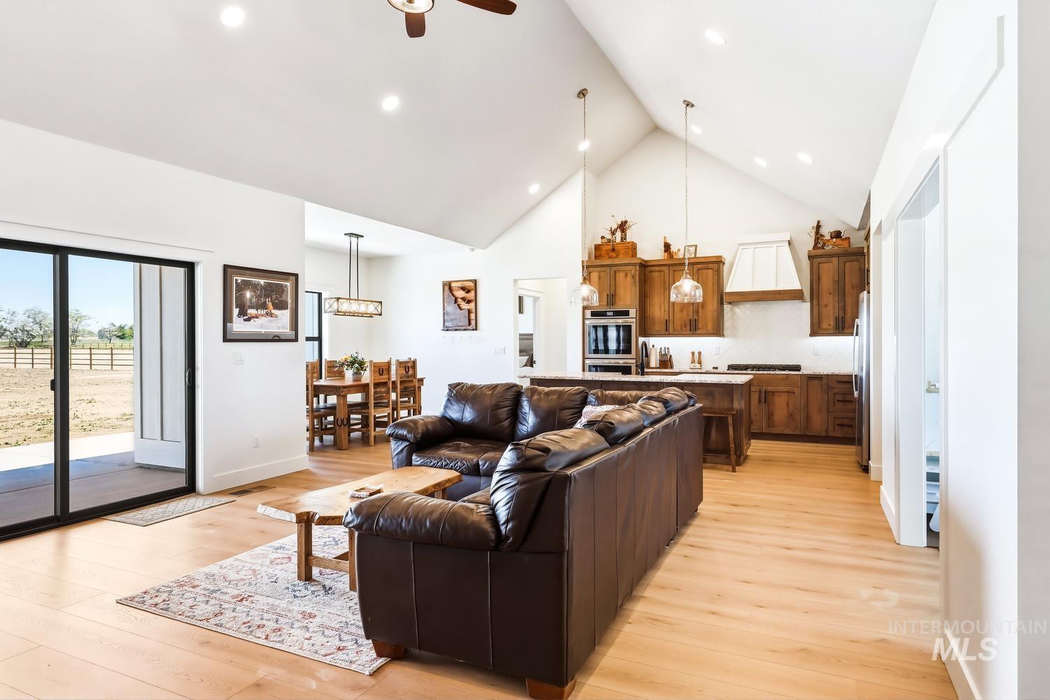 18658 Tranquil Place Caldwell, ID 83607 - Photo 5 of 44 Vaulted ceiling main living area featuring wood-finish flooring, a kitchen with custom wood cabinetry and stainless steel appliances, a dining area with a linear chandelier, and a sliding glass door opening to an outdoor space